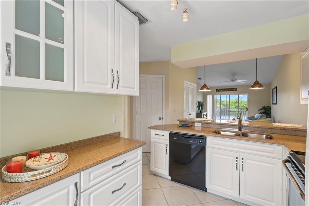 Kitchen with white cabinets, glass insert cabinets, black dishwasher, light stone counters, and light tile patterned floors