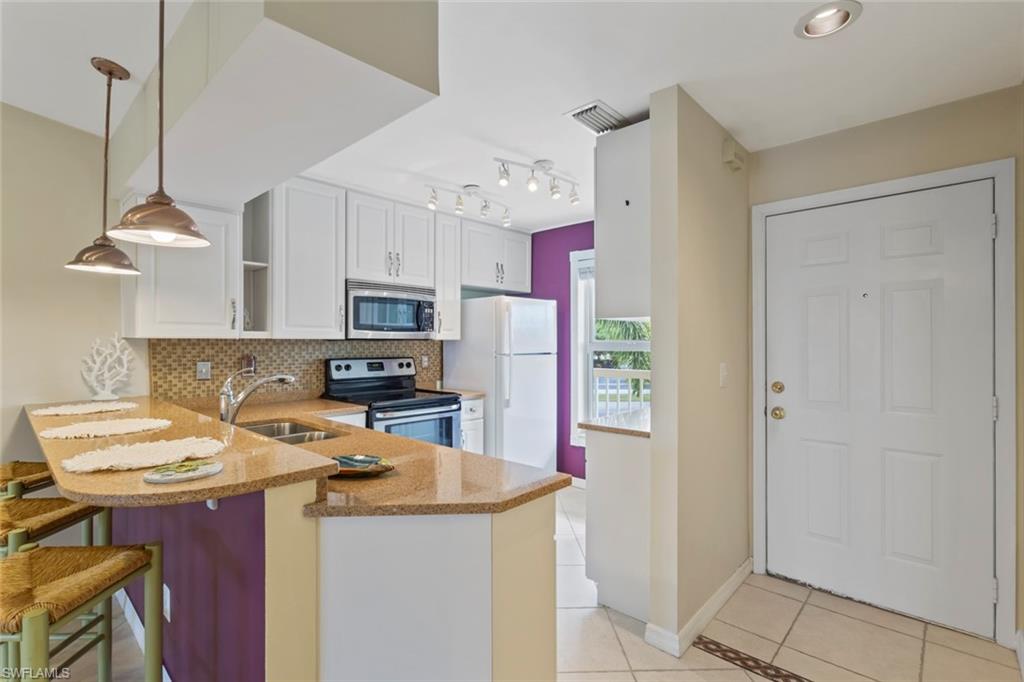 Kitchen featuring light tile patterned flooring, decorative backsplash, a peninsula, appliances with stainless steel finishes, and light stone counters
