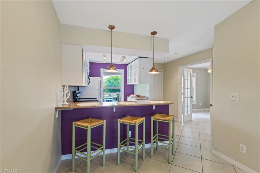 Kitchen featuring a kitchen bar, white cabinets, a peninsula, light tile patterned floors, and pendant lighting