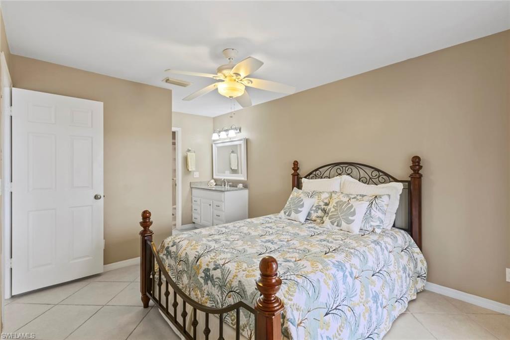 Bedroom with light tile patterned floors, connected bathroom, and ceiling fan