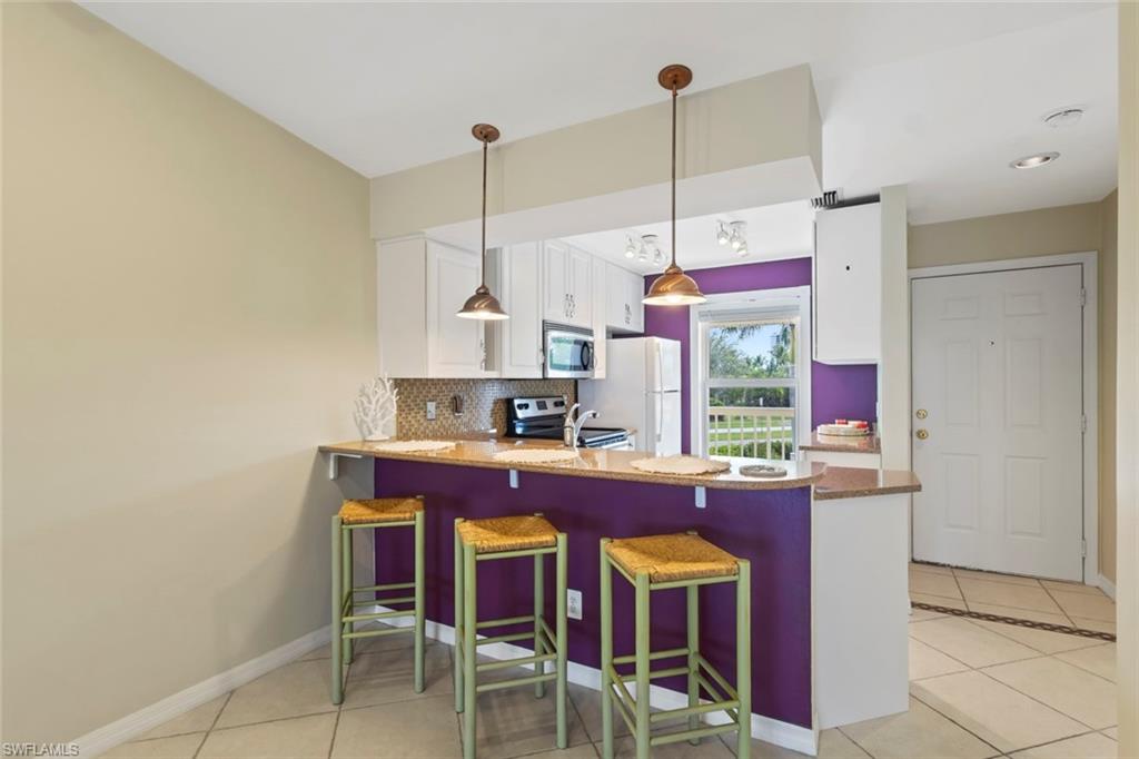 Kitchen with a breakfast bar area, light tile patterned floors, a peninsula, white cabinets, and backsplash