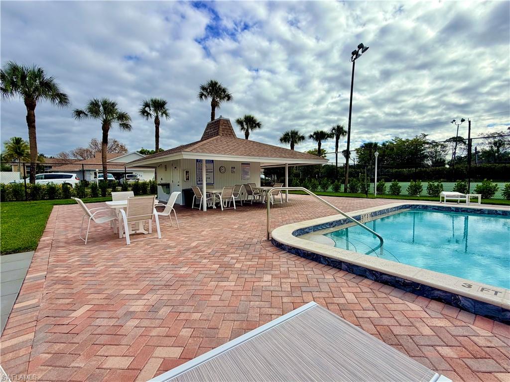 Swimming pool area featuring a brick paver deck, a covered pavilion, and mature palm trees