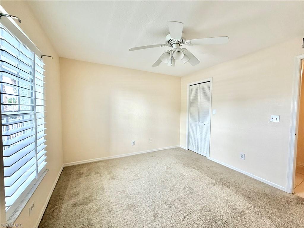 Guest Carpeted interior room featuring light-toned walls, a louvered window with privacy blinds, a white ceiling fan with integrated lighting, and bi-fold closet doors