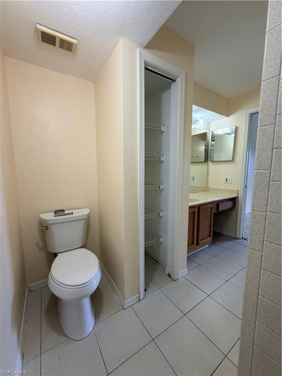 Bathroom featuring a white toilet, tile flooring, an open closet with wire shelving, and a vanity with a wood-finish cabinet and light-toned countertop