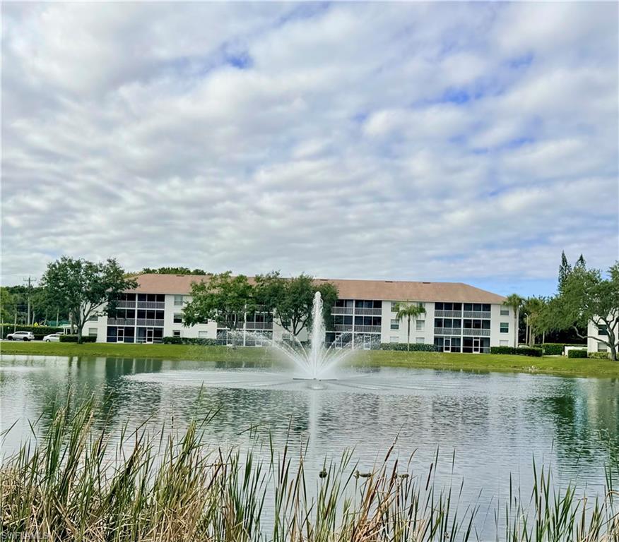 Waterfront condominium building featuring multiple screened balconies, a central fountain, and lush perimeter landscaping