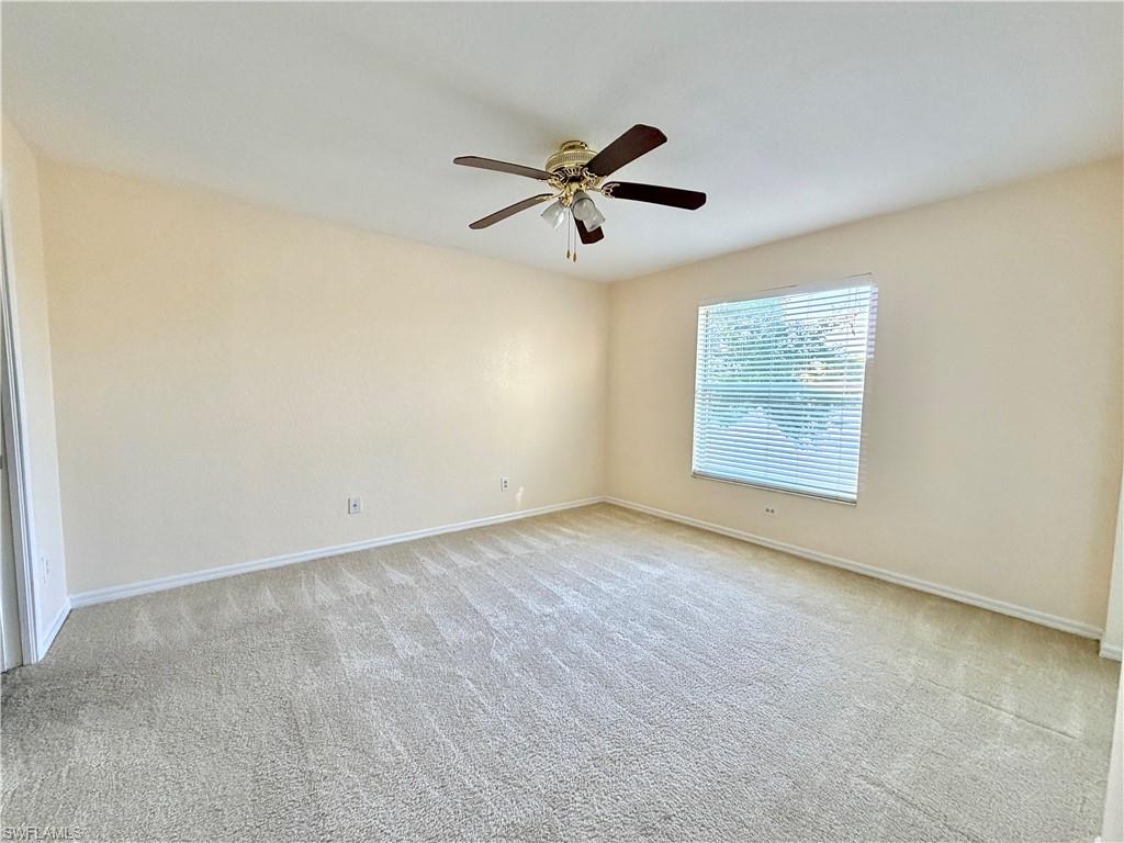Carpeted interior space featuring a window with blinds, a ceiling fan with light fixture, and neutral-toned walls