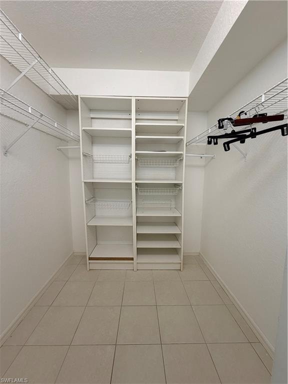 Walk-in closet featuring built-in white shelving, wire shelving, hanging rods, and tile flooring