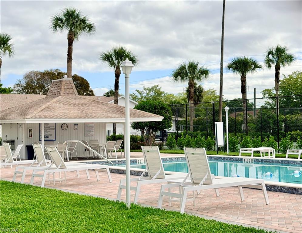 Resort-style pool area featuring a rectangular pool, paver deck, surrounding lawn, and palm trees