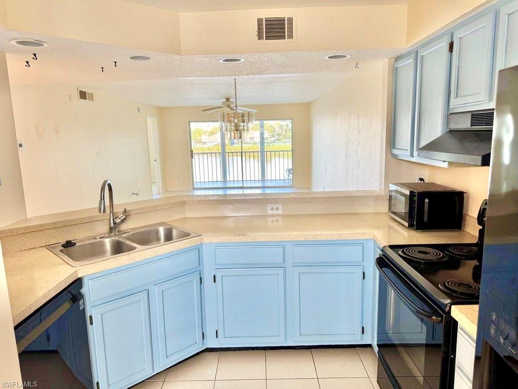 Kitchen with black appliances, range hood, light countertops, a textured ceiling, and blue cabinetry
