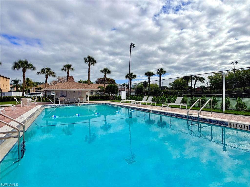 Resort-style swimming pool featuring a brick paver deck, palm trees, and a pool house