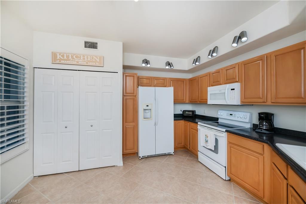 Kitchen with white appliances, light tile patterned flooring, and brown cabinetry