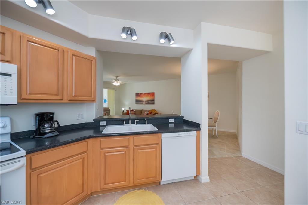 Kitchen with white appliances, light tile patterned flooring, a ceiling fan, open floor plan, and dark stone countertops