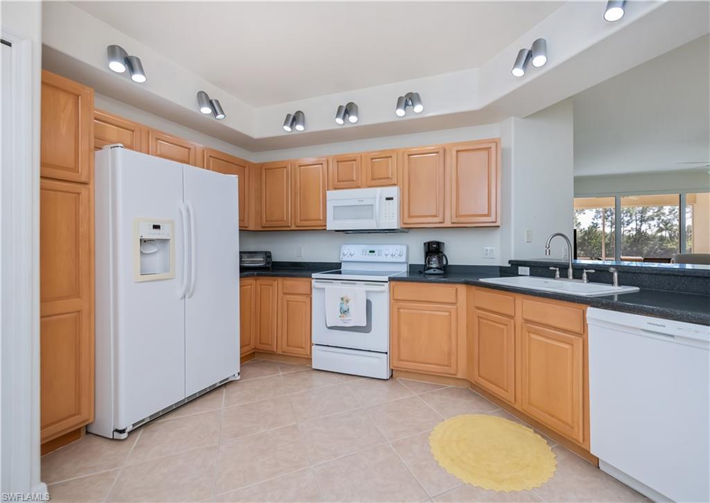 Kitchen with white appliances, light tile patterned flooring, and light brown cabinets