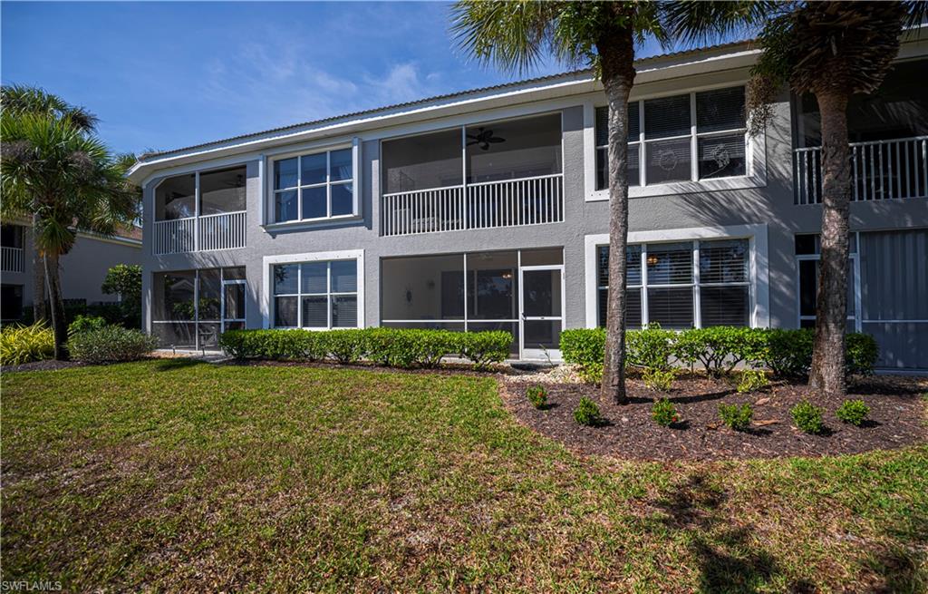 Rear view of property with stucco siding, a sunroom, a balcony, and a lawn