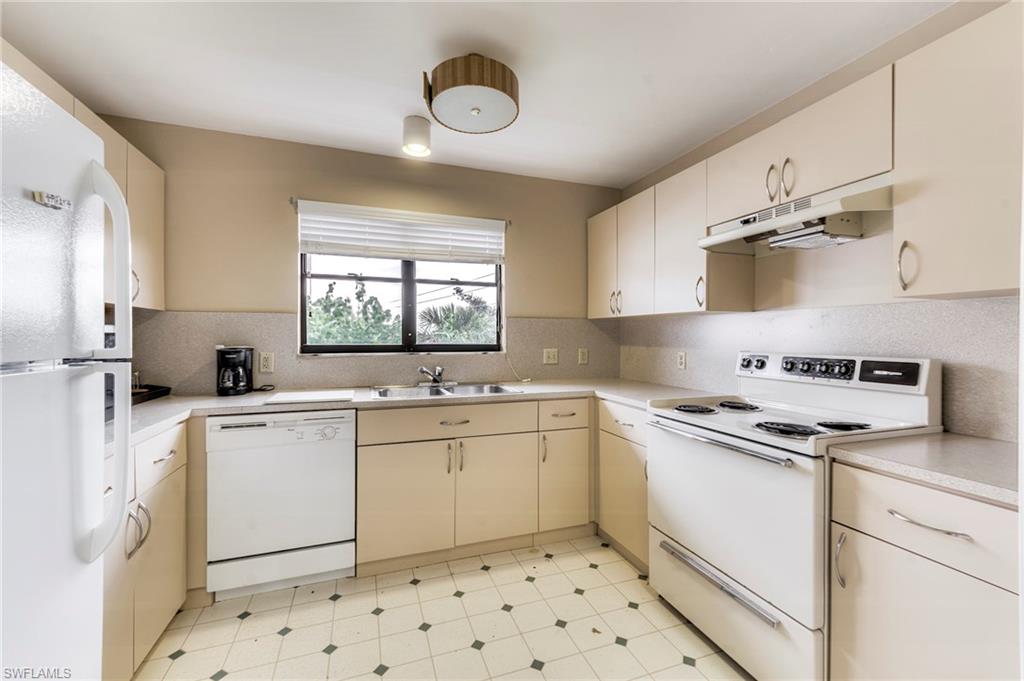 Kitchen featuring white appliances, light countertops, under cabinet range hood, cream cabinetry, and tasteful backsplash
