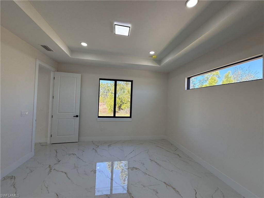 Empty room featuring recessed lighting, a raised ceiling, and light marble finish floors