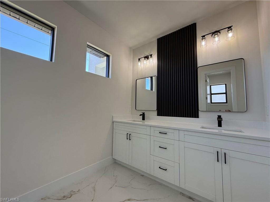 Full bathroom with double vanity, light marble finish floors, and healthy amount of natural light