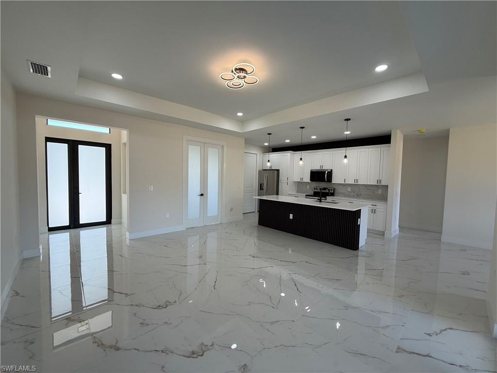 Unfurnished living room with french doors, a raised ceiling, recessed lighting, and light marble finish flooring