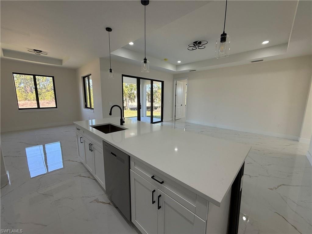 Kitchen featuring open floor plan, a tray ceiling, white cabinetry, hanging light fixtures, and stainless steel dishwasher