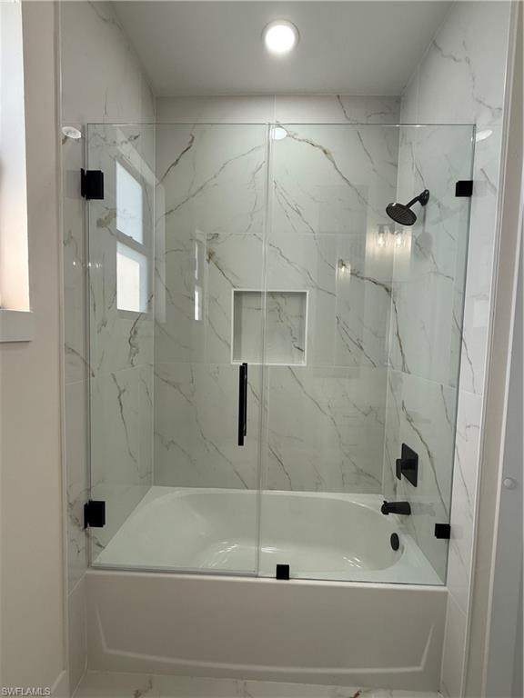 Bathroom with marble finish flooring and bath / shower combo with glass door