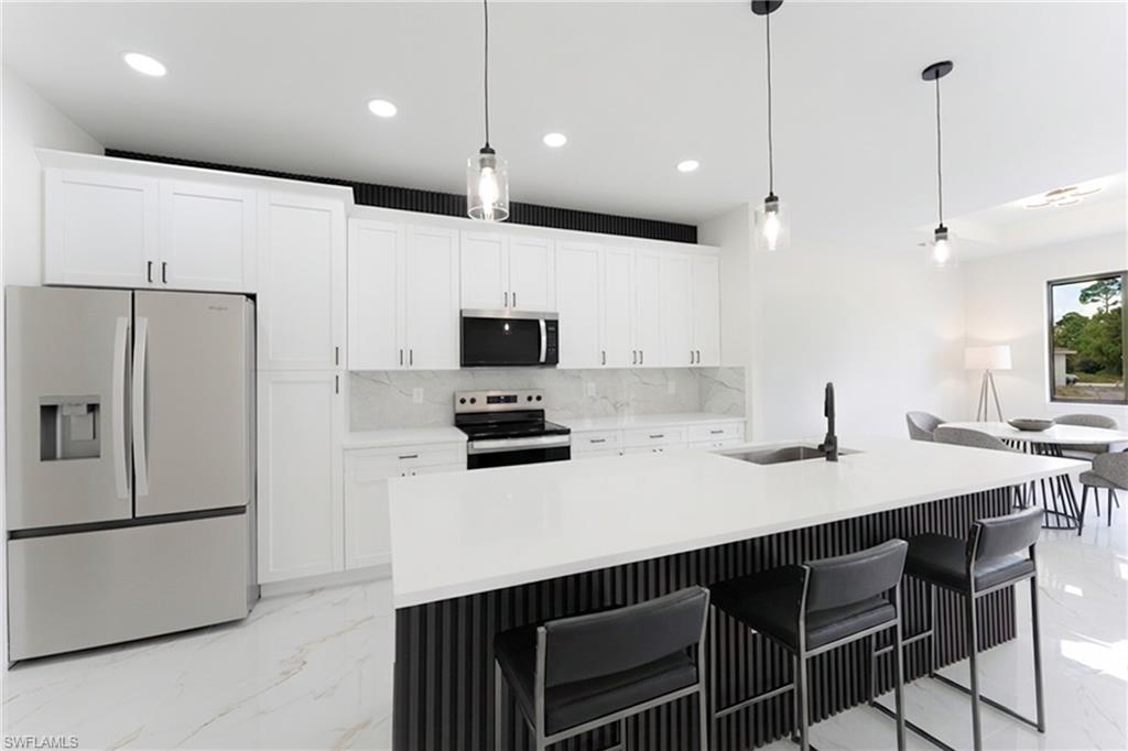 Kitchen with stainless steel appliances, a breakfast bar, white cabinetry, an island with sink, and decorative light fixtures