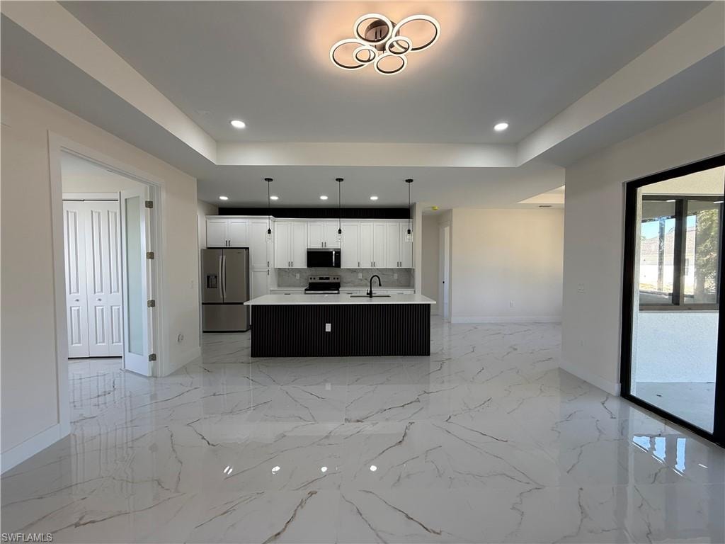 Kitchen with open floor plan, stainless steel appliances, an island with sink, pendant lighting, and white cabinets