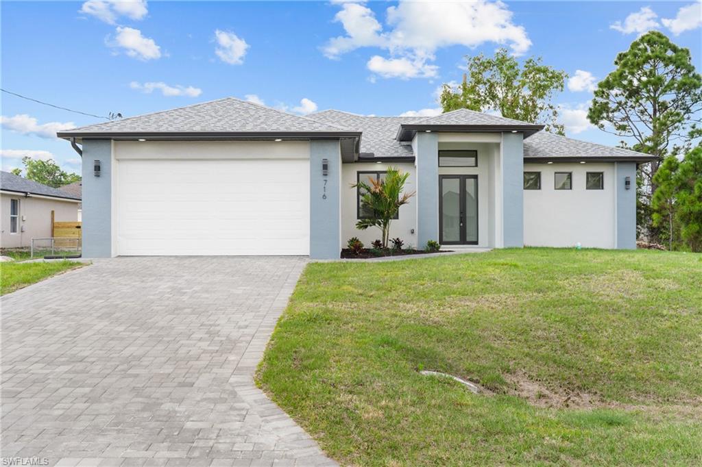 Prairie-style home featuring stucco siding, an attached garage, decorative driveway, and a front lawn