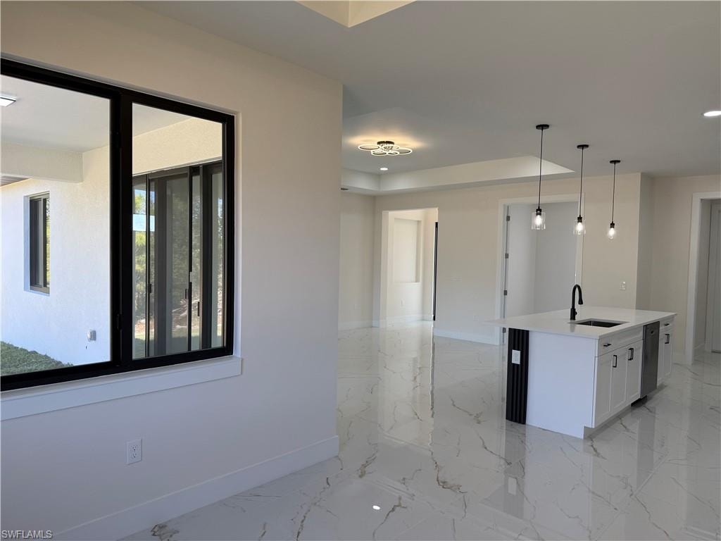 Kitchen featuring a center island with sink, decorative light fixtures, light stone counters, white cabinetry, and open floor plan