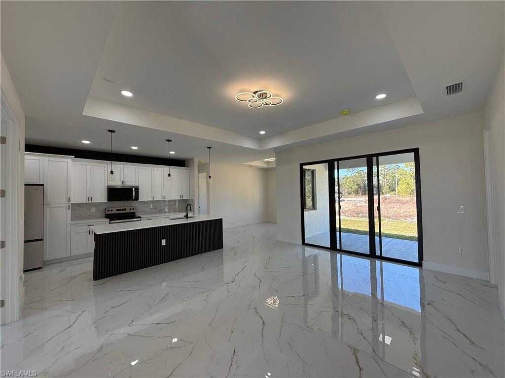 Kitchen with open floor plan, a center island with sink, white cabinetry, hanging light fixtures, and stainless steel appliances