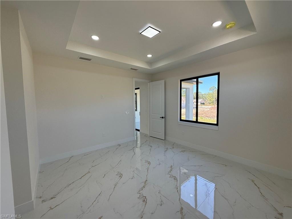 Spare room with recessed lighting, light marble finish floors, and a raised ceiling