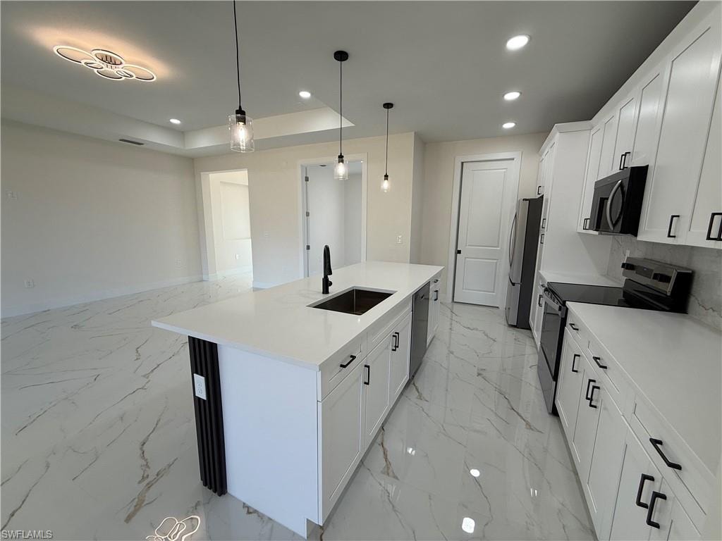 Kitchen featuring white cabinets, stainless steel appliances, decorative light fixtures, a center island with sink, and light stone countertops