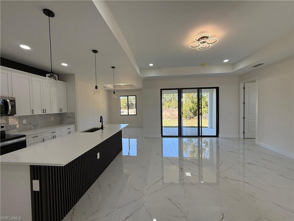 Kitchen featuring hanging light fixtures, white cabinetry, stainless steel appliances, an island with sink, and open floor plan