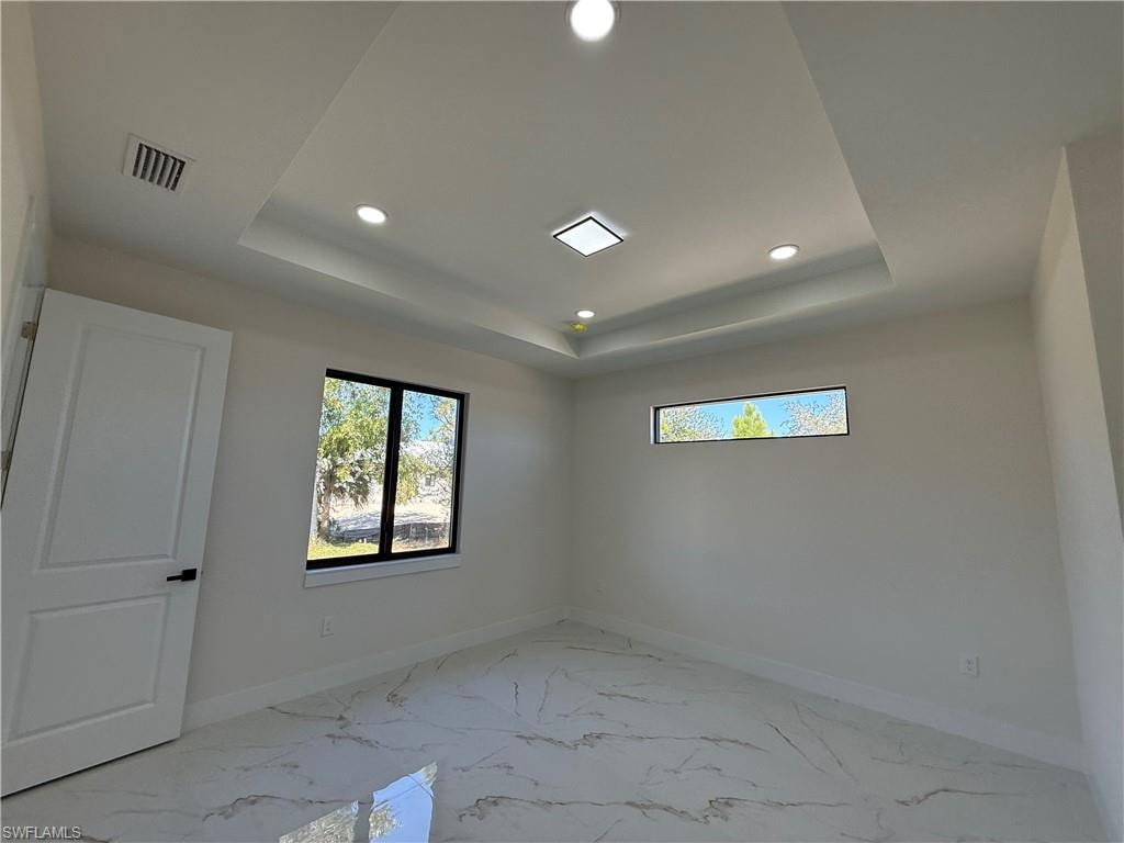 Spare room featuring light marble finish flooring, recessed lighting, and a tray ceiling