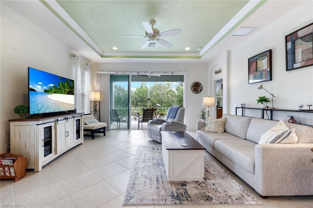 Living area with light tile patterned floors, a tray ceiling, a ceiling fan, recessed lighting, and ornamental molding