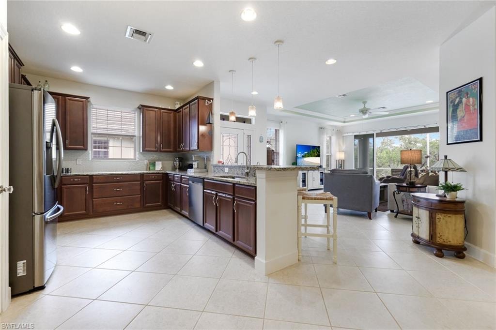Kitchen featuring appliances with stainless steel finishes, light stone countertops, a raised ceiling, backsplash, and brown cabinetry