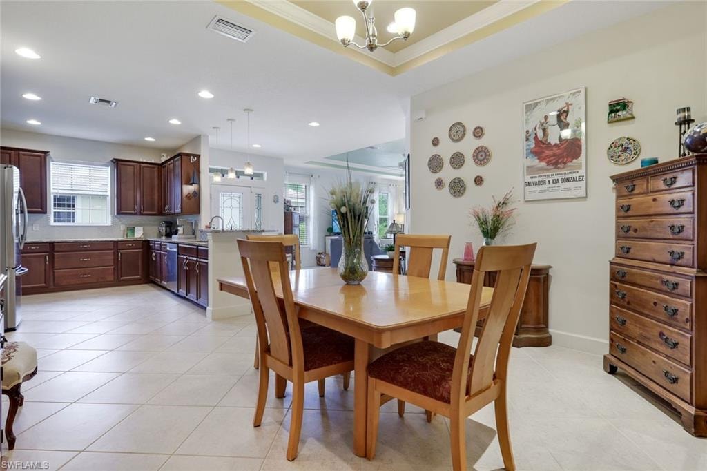 Dining space featuring a tray ceiling, recessed lighting, arched walkways, crown molding, and light tile patterned floors