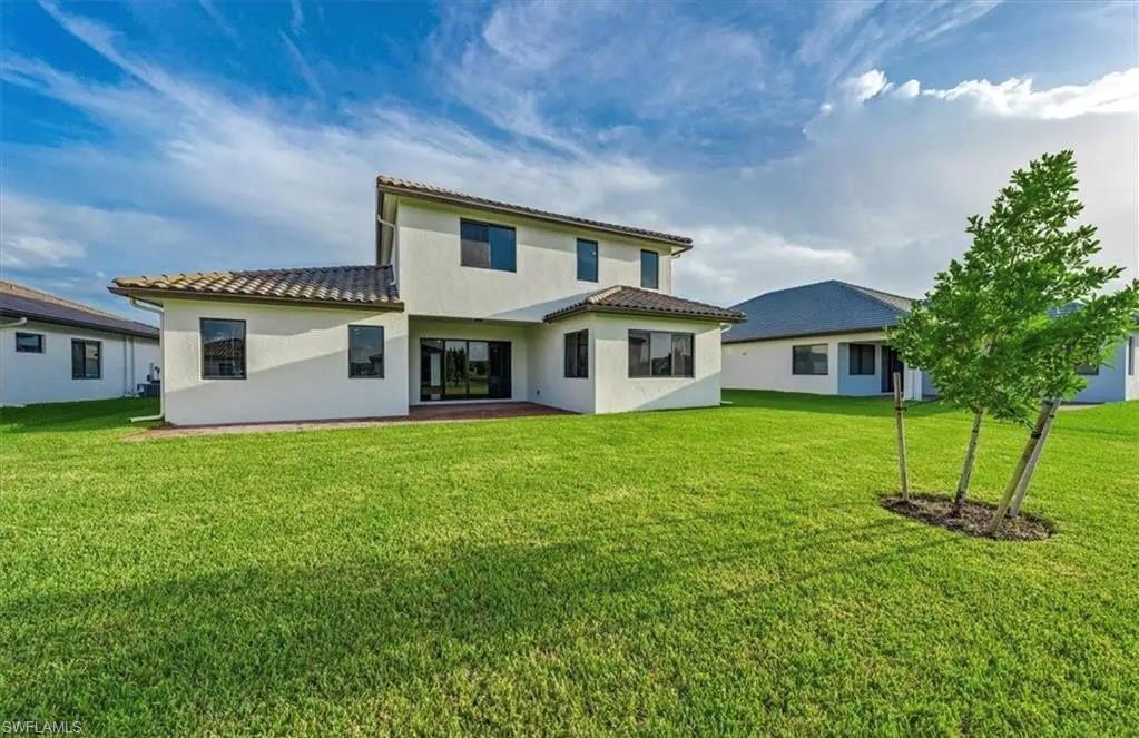 Rear view of property featuring a yard, stucco siding, a tiled roof, and a patio