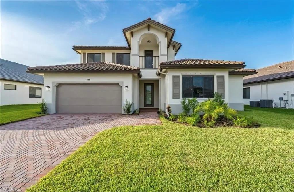 Mediterranean / spanish-style home featuring a garage, stucco siding, a front yard, and driveway