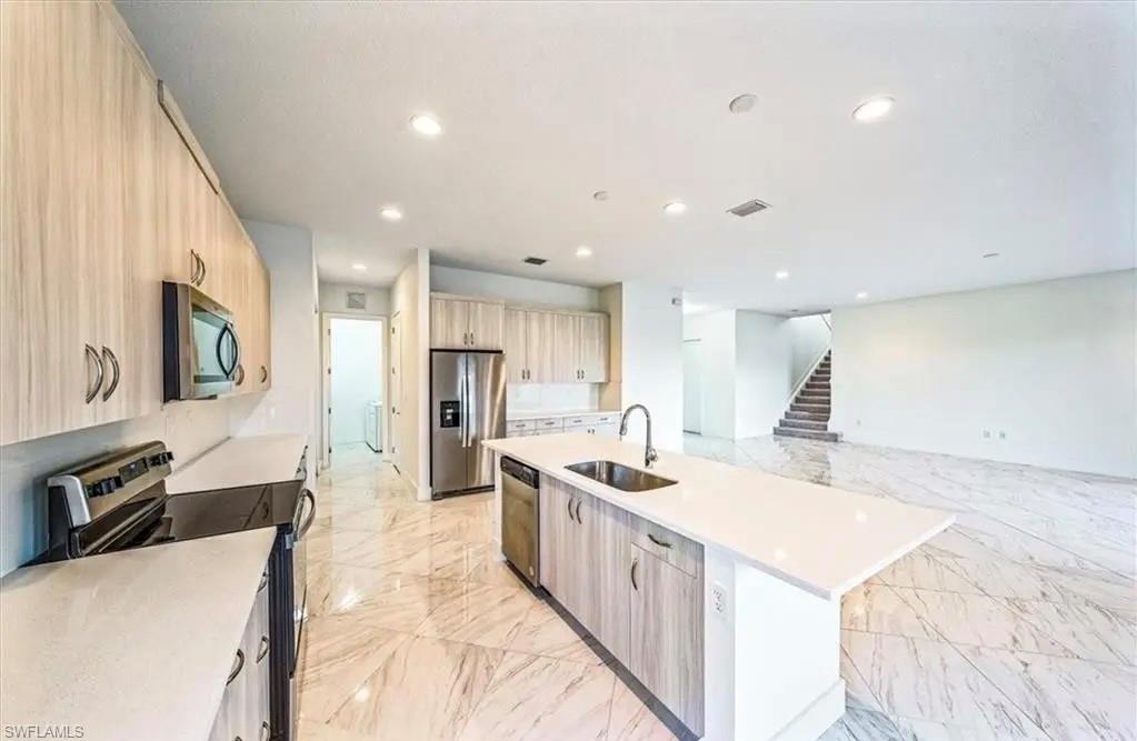 Kitchen featuring appliances with stainless steel finishes, light stone counters, an island with sink, recessed lighting, and light marble finish flooring