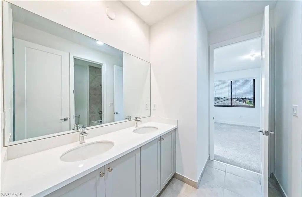 Bathroom with double vanity, light tile patterned floors, and light colored carpet