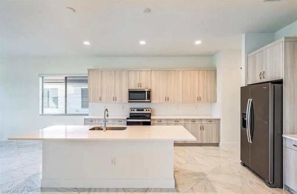 Kitchen featuring appliances with stainless steel finishes, light marble finish flooring, a center island with sink, light stone countertops, and recessed lighting