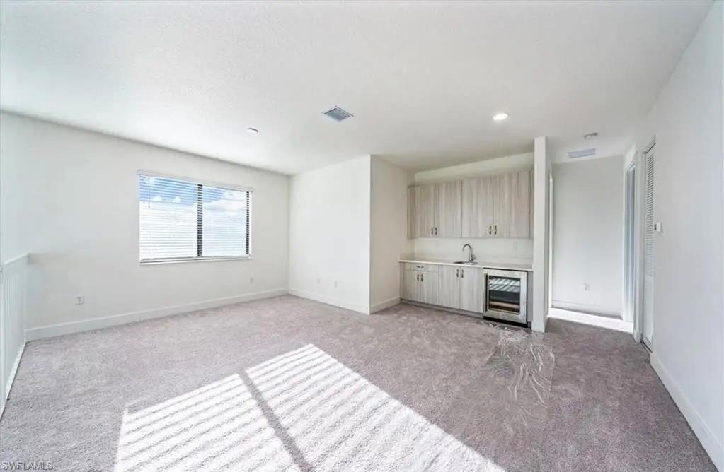 Unfurnished living room featuring light colored carpet, beverage cooler, wet bar, and recessed lighting