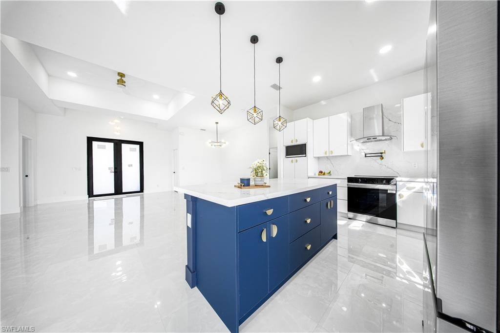 Kitchen with white cabinets, stainless steel range with electric stovetop, pendant lighting, blue cabinets, and a kitchen island
