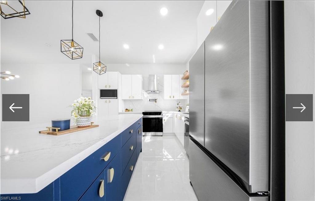 Kitchen with stainless steel appliances, pendant lighting, dual tone cabinetry, light stone countertops, and extractor fan