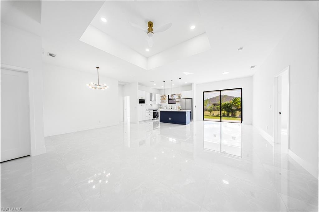 Unfurnished living room featuring a raised ceiling, ceiling fan, a chandelier, and recessed lighting