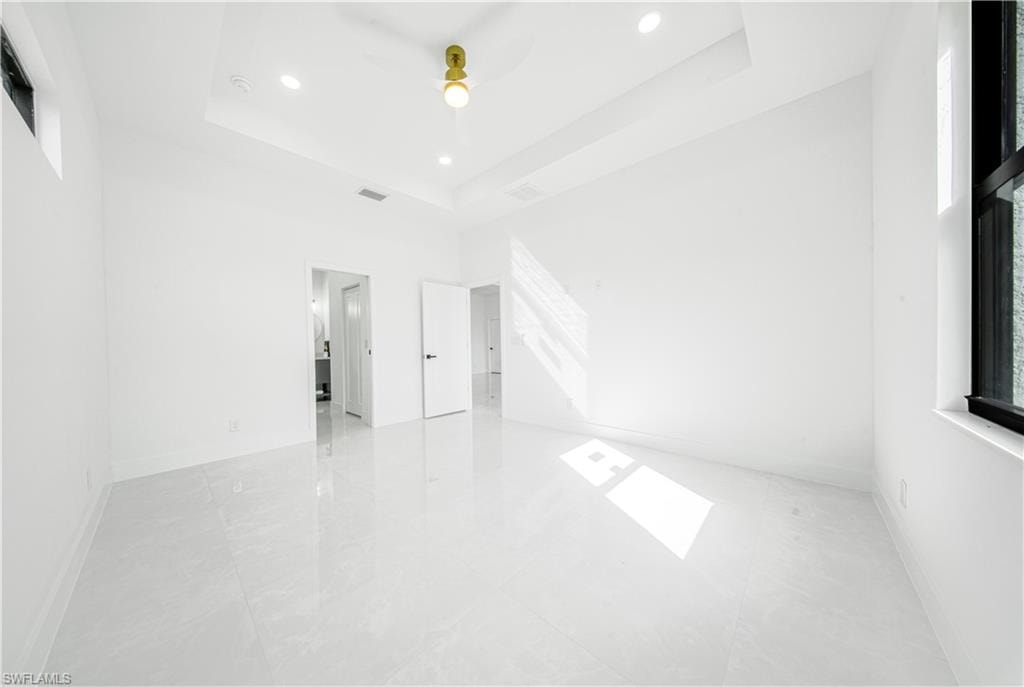 Spare room with a raised ceiling, recessed lighting, a ceiling fan, and light tile patterned floors