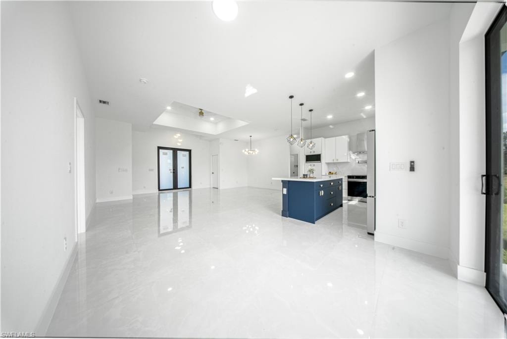 Unfurnished living room with a raised ceiling, french doors, recessed lighting, and a chandelier