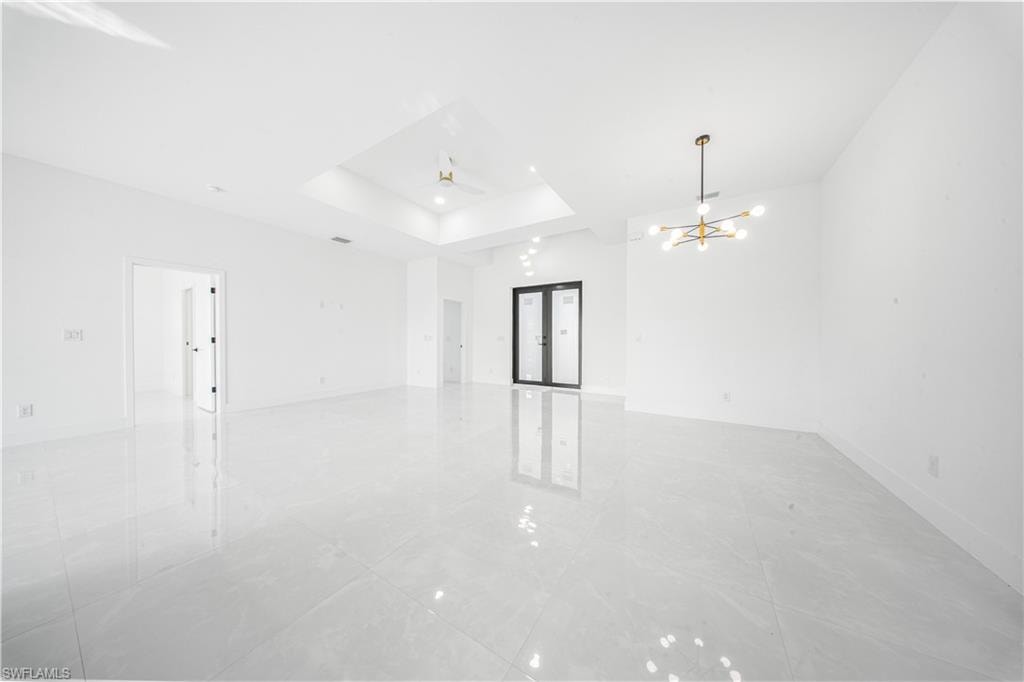 Empty room with french doors, a tray ceiling, and a chandelier