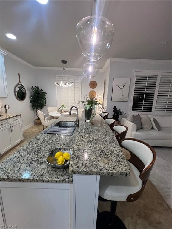 Kitchen with dark stone counters, a breakfast bar, ornamental molding, white cabinets, and a center island with sink