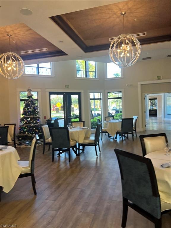 Dining area with a chandelier, a high ceiling, a tray ceiling, wood finished floors, and healthy amount of natural light